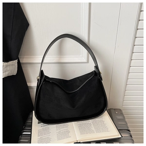 Détail d'un sac sous les bras en daim noir sur une valise argentée avec un livre