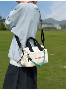 Bolso bandolera de nailon blanco con detalle de cuerda verde y correa negra al aire libre