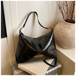 Dettaglio borsa tote in pelle cerata nera con logo dorato e tracolla larga su libri vintage