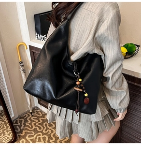 Detail of a large black faux leather tote bag with an ethnic style beaded tassel charm