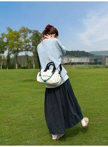 Bolso bandolera de lona blanca con texto rojo y detalle de cuerda verde al aire libre