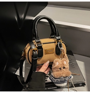 Dettaglio borsa Boston scamosciata marrone con manici in pelle nera e ciondolo a cane