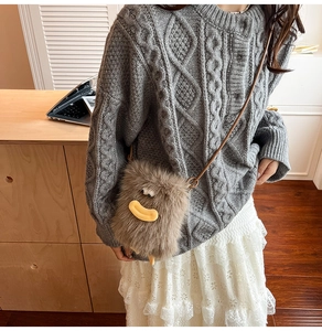 Brown plush cartoon crossbody bag with eyes and leather strap worn with grey knit sweater
