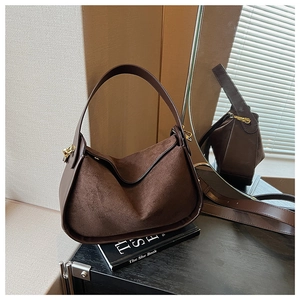 Détail du sac selle en daim marron foncé avec boucle métallique dorée et texture cuir