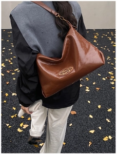Dettaglio della borsa a tracolla in pelle marrone con logo dorato e stile autunnale
