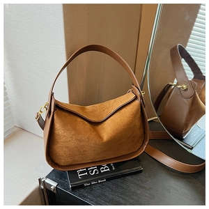 Détail du sac à bandoulière en daim et cuir avec accessoires dorés sur un bureau