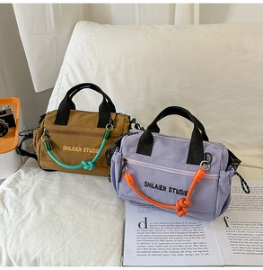 Detalle de bolsos bandolera de lona en marrón y lila con asa de cuerda y bolsillo con cremallera