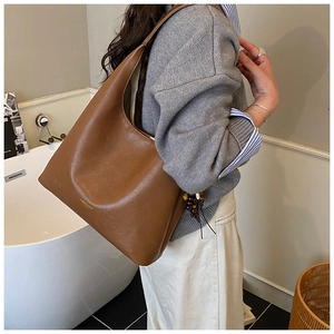 Grand sac hobo en cuir marron avec logo doré et pendentif perlé porté à l'épaule