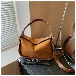 Gros plan d'un sac bandoulière en daim caramel avec poignées en cuir lisse et boucles métal