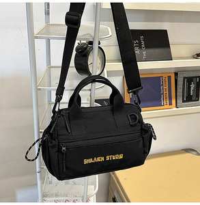 Detalle de bandolera de lona negra con bordado amarillo y cordón de estilo técnico