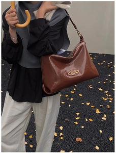 Dettaglio della borsa hobo in pelle marrone lucida con logo oro e tracolla larga