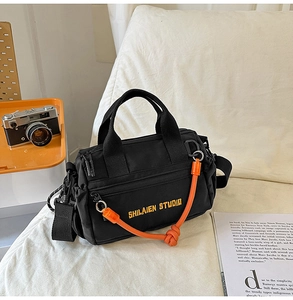 Detalle del bolso bandolera de nailon negro con cordón naranja y bordado moderno