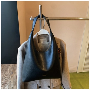 Détail du sac cabas en cuir noir avec logo sur un fond de manteau en laine grise