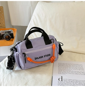 Detalle de bolso bandolera de nailon morado con cuerda naranja y bolsillos laterales