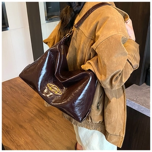 Dettaglio della borsa tote in vernice marrone scuro con finiture dorate e tracolla larga