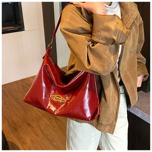 Dettaglio borsa hobo in vernice rossa con logo ovale giallo e fibbia metallica