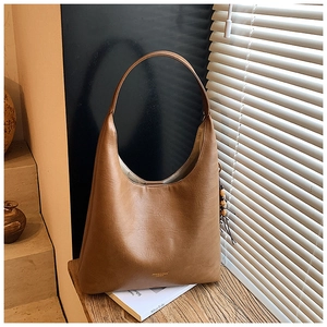Détail du sac hobo marron montrant la texture cuir, logo doré et pendentif en bois