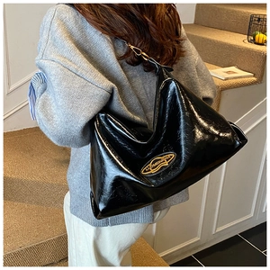 Dettaglio della borsa tote in pelle nera lucida con tracolla e logo dorato