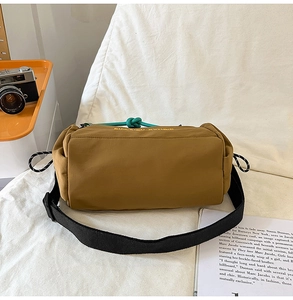 Detalle de bolso bandolera cilíndrico de nailon marrón con nudo verde y bordado