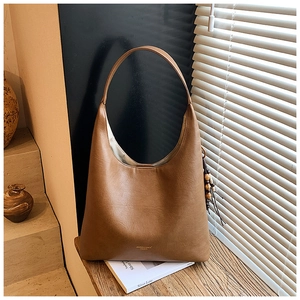 Détail du sac hobo en cuir mat marron avec pompon sur une table en bois texturé