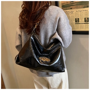 Dettaglio di una grande borsa tote in pelle verniciata nera con logo dorato sulla spalla