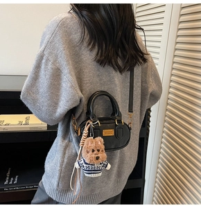 Detail of black leather Boston bag featuring a cute plush dog charm and gold hardware