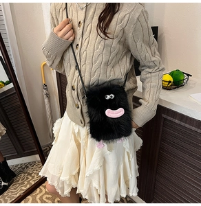 Detail of a fluffy black monster plush crossbody bag with cartoon eyes and pink lips