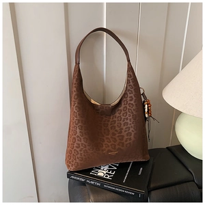 Détail du sac hobo léopard avec pendentif à pompon et logo de marque doré au bas