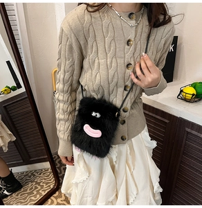 Detail of cute black plush crossbody bag with cartoon eyes on beige knit sweater