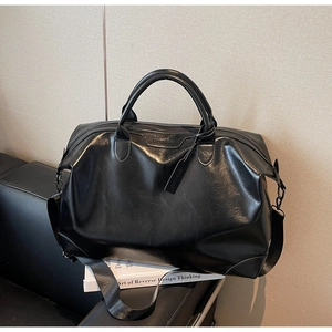 Détail du grand sac de voyage noir avec doubles poignées et bandoulière sur un canapé