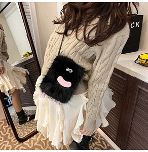 Detail of cute black plush monster crossbody bag with large eyes and pink tongue feature