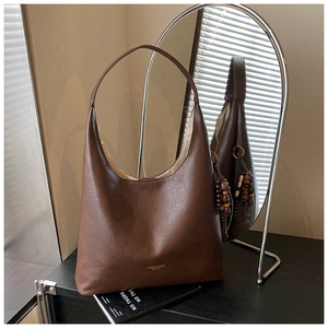 Détail du sac cabas café noir avec texture lisse et breloque en bois sur une table épurée