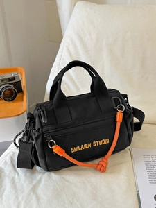 Bolso bandolera de nailon negro con bordado naranja y nudo decorativo en fondo blanco
