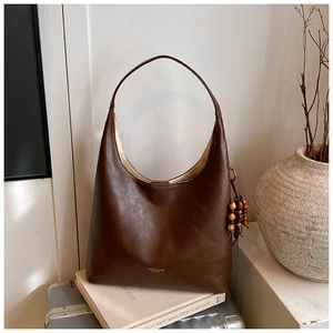 Détail du sac hobo en cuir marron foncé avec logo doré et pompon en perles de bois