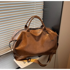 Détail d'un grand sac de voyage en cuir marron avec poignées renforcées et bandoulière