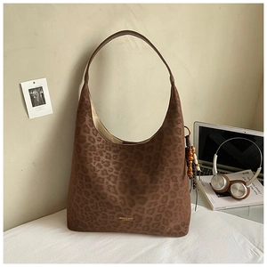 Détail du sac hobo léopard avec pompon en perles de bois et logo de marque sur le fond