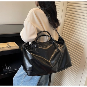 Modèle portant un grand sac cabas en cuir noir avec une large bandoulière en bandoulière
