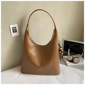 Détail du sac hobo en cuir marron caramel avec texte doré et pendentif en perles