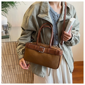 Close-up of brown suede and leather shoulder bag with silver buckle held by a model