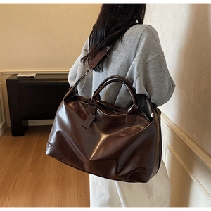 Détail d'un sac cabas marron foncé montrant le cuir huilé brillant et la bandoulière