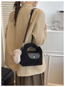 Detail of a black plush crossbody bag featuring a leather flap and white bunny charm accessory