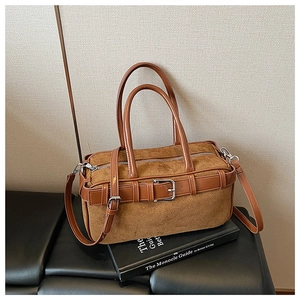 Close-up of brown suede bucket bag with leather strap detail on a lifestyle book