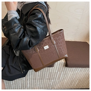 Détail d'un sac cabas imprimé léopard avec bordures en cuir et plaque logo métallique