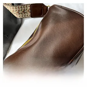 Detail of dark brown lychee leather grain with colorful retro woven shoulder strap