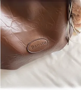 Detail of dark brown wrinkled leather texture and embossed Banatu logo on a tote bag