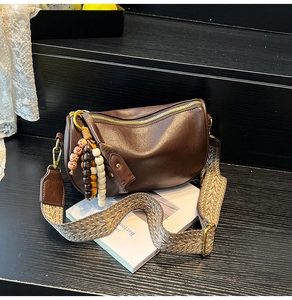 Detail of dark brown boston bag featuring wide woven strap and vintage wooden bead charm