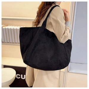 Close-up of a large black suede tote bag with wide straps worn by a model in a beige coat