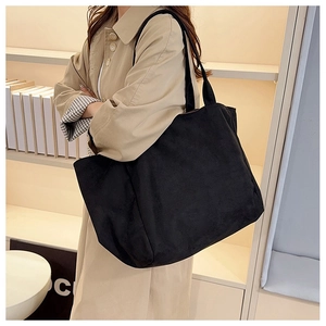 Detail view of the large black minimalist tote bag carried by a model in a trench coat