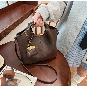 Détail du sac seau marron foncé avec texture litchi et mini breloque de sac sur une table