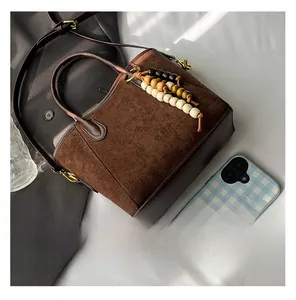 Détail du sac seau en daim marron avec garniture en cuir et breloque en bois